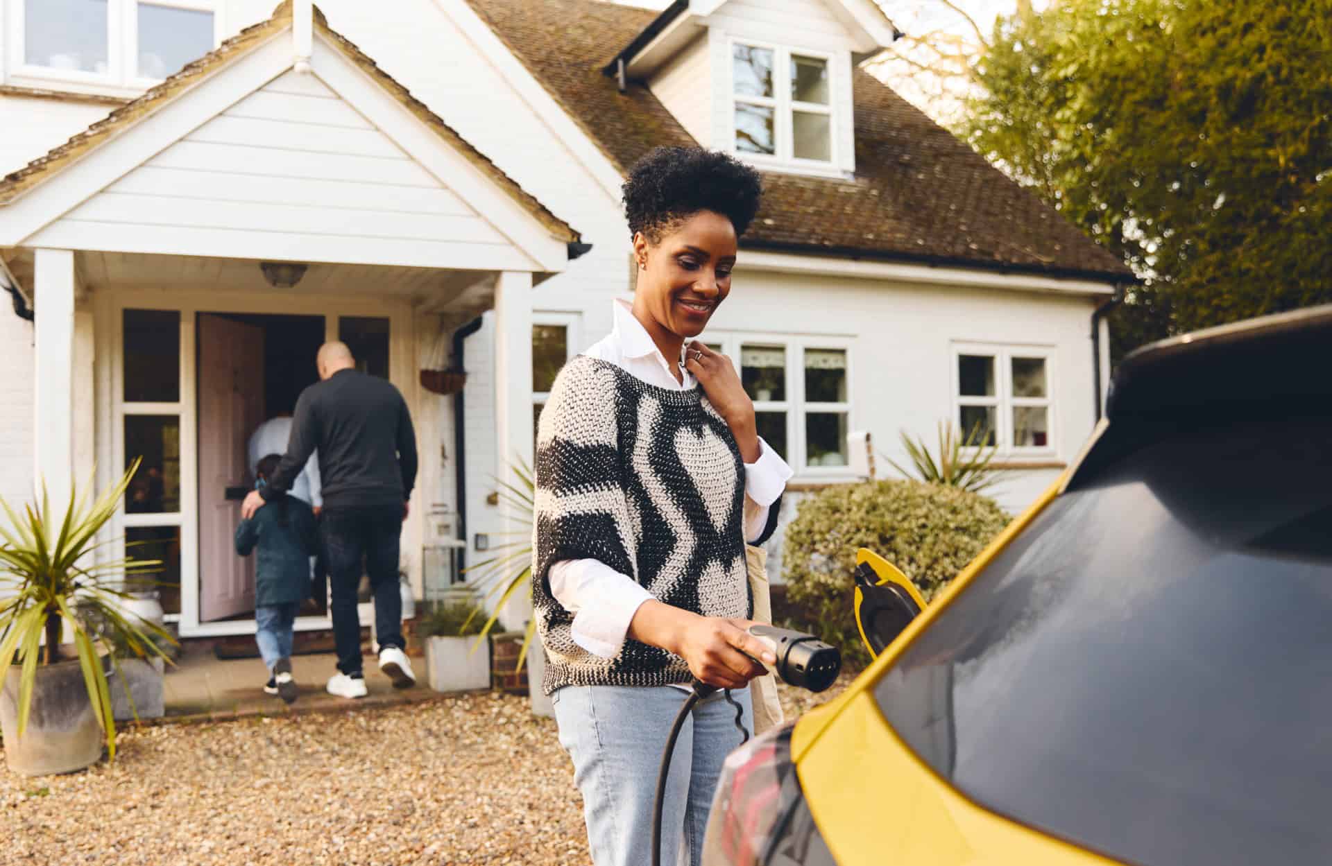 Woman plugging in electric charger into car with family outside